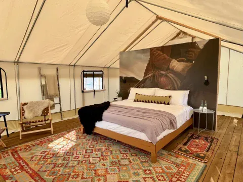 Safari tent interior with a bed, seating, and Western decor